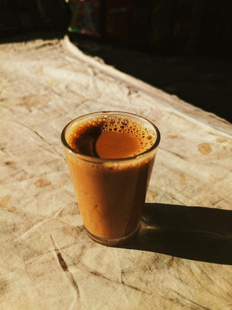 Home A steaming glass of masala chai casting a long shadow in warm sunlight on a rustic cloth surface.